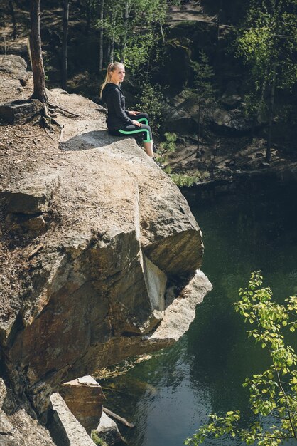 Beautiful blonde woman enjoying blue lake water on the high cliff in summer