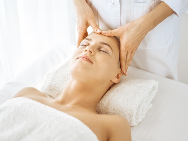 Beautiful blonde woman enjoying facial massage with closed eyes. Relaxing treatment in medicine and spa center concepts.