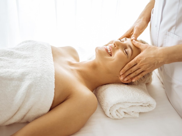 Beautiful blonde woman enjoying facial massage with closed eyes. Relaxing treatment in medicine and spa center concepts.