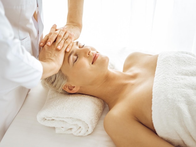 Beautiful blonde woman enjoying facial massage with closed eyes. Relaxing treatment in medicine and spa center concepts.