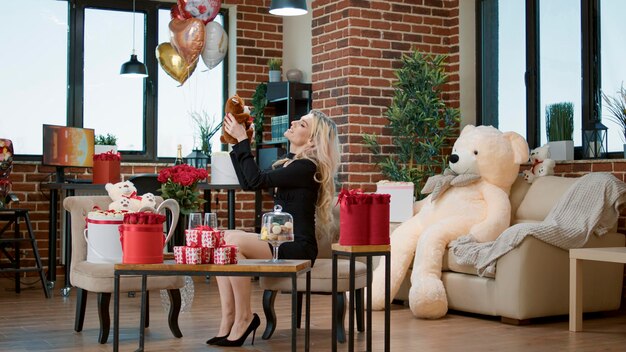 Beautiful blonde woman enjoying valentines day surprise with flowers and gifts. Sexy attractive girl feeling happy about roses bouquet and teddy bear present to celebrate romantic holiday.