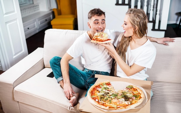 Beautiful blonde woman feeding boyfriend with pizza