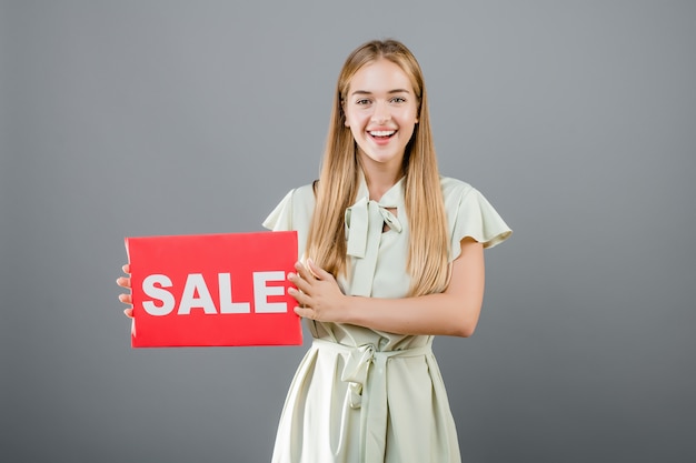 Beautiful blonde woman has sale sign isolated over grey