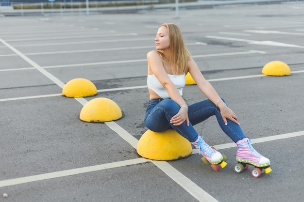 Beautiful blonde woman in jeans in rollers sitting on parking