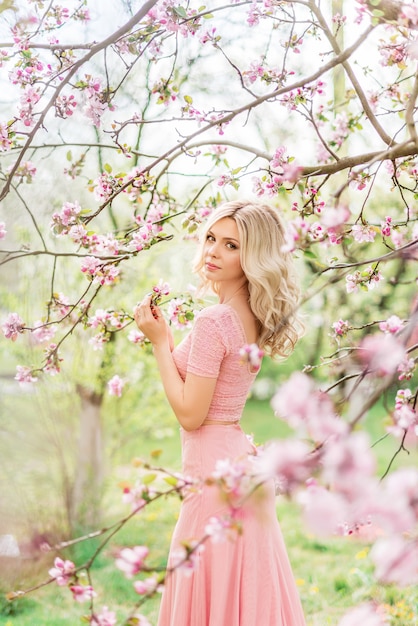 Beautiful blonde woman in a pink long dress in a spring blooming garden