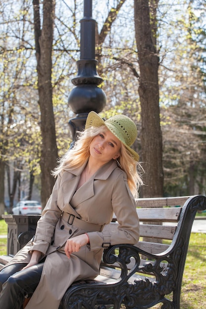 Foto bella donna bionda in un impermeabile e cappello si siede su una panchina