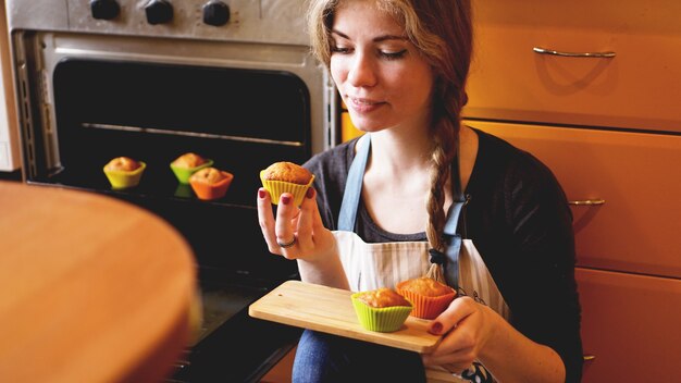 キッチンでマフィンを見せている美しいブロンドの女性。料理と家のコンセプト