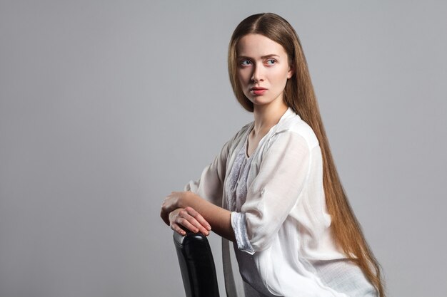 Beautiful blonde woman sitting on gray background