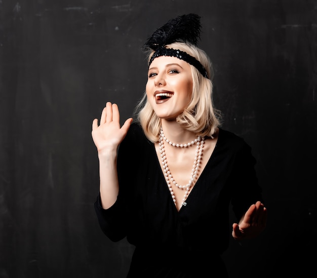 Beautiful blonde woman in twenties years clothes dancing on dark background