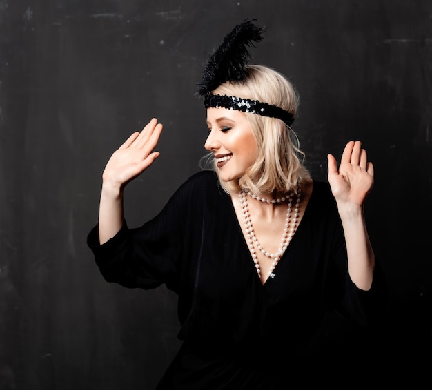 Beautiful blonde woman in twenties years clothes dancing on dark background