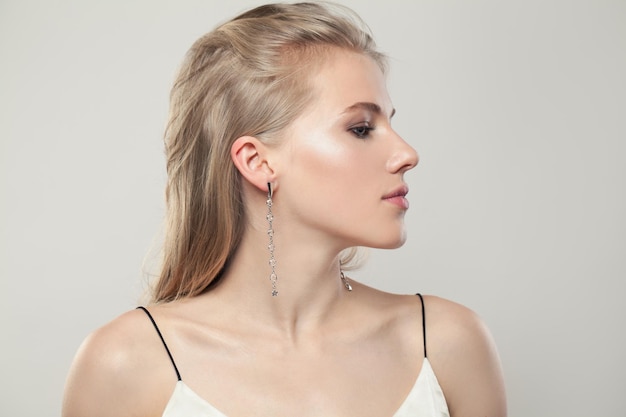 Beautiful blonde woman wearing silver earrings with diamonds on white background portrait