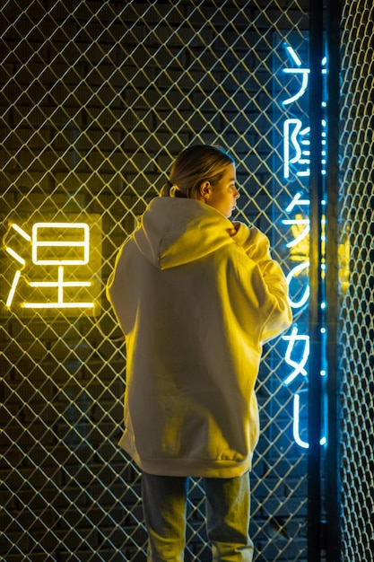 Photo beautiful blonde woman in white hoodie and blue jeans posing against neon background