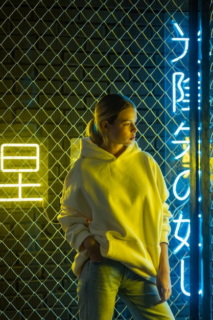 Photo beautiful blonde woman in white hoodie and blue jeans posing against neon background