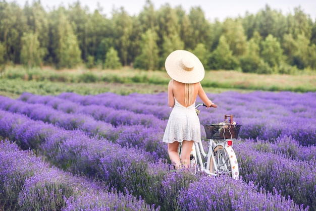 Beautiful blonde woman with a bicycle in lavender. View from the back.