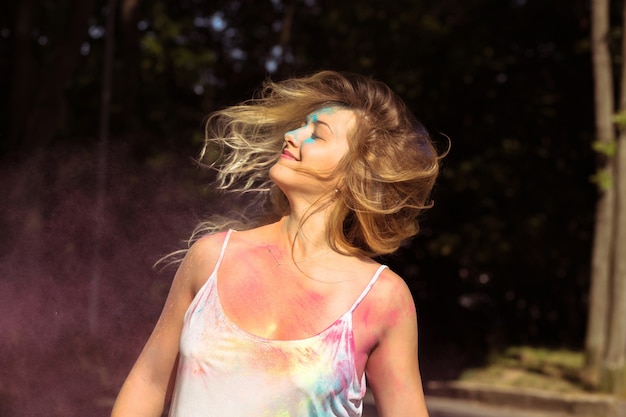 Beautiful blonde woman with long hair fluttering on wind with pink Holi dry powder