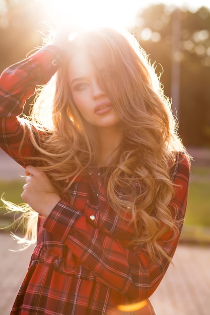 Beautiful blonde woman with long wavy hair in fashionable checkered dress