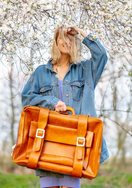 Beautiful blonde woman with suitcase next to blooming tree