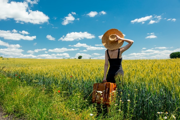 Beautiful blonde woman with suitcase in countryside road near wheat field
