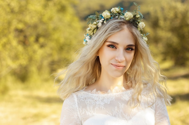 Beautiful blonde young bride portrait with flower bouquet and wreath on her head in white wedding