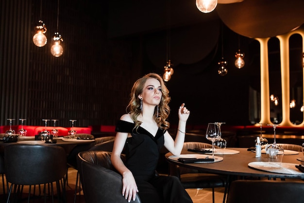 Beautiful blonde young girl Portrait of a young girl in a restaurant Young girl in a restaurant on a black background Portrait of a girl in a black dress Young girl