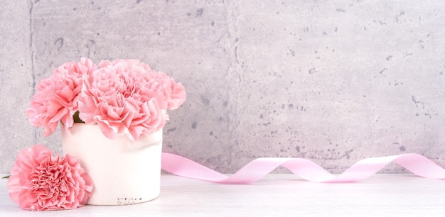 Beautiful blooming carnations with pink ribbon box isolated on fair-faced gray background desk, close up, copy space