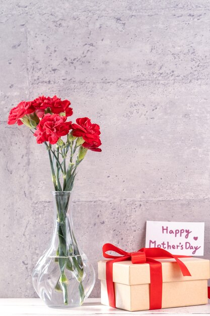 Beautiful blooming carnations with red ribbon box isolated on fair-faced gray background desk, close up, copy space