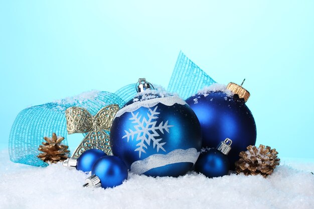 Beautiful blue Christmas balls and cones in snow on blue background