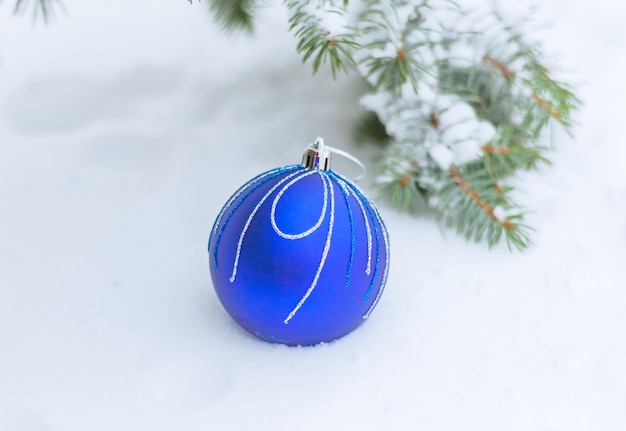 a beautiful blue Christmas bauble lies on natural snow near a spruce branch