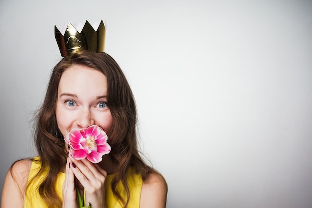 Bella ragazza dagli occhi azzurri che tiene in mano un fiore rosa, sorridente, con indosso una corona d'oro