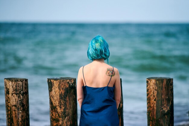 Photo beautiful blue-haired woman in long dark blue dress with cute tattoo on her shoulder blade on beach