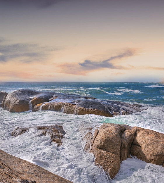 Beautiful blue ocean view of a sea with a light colorful sky copy space Outdoor landscape of rocks and waves in nature on a summer beach day Relaxing coastal setting outside with the sun shining