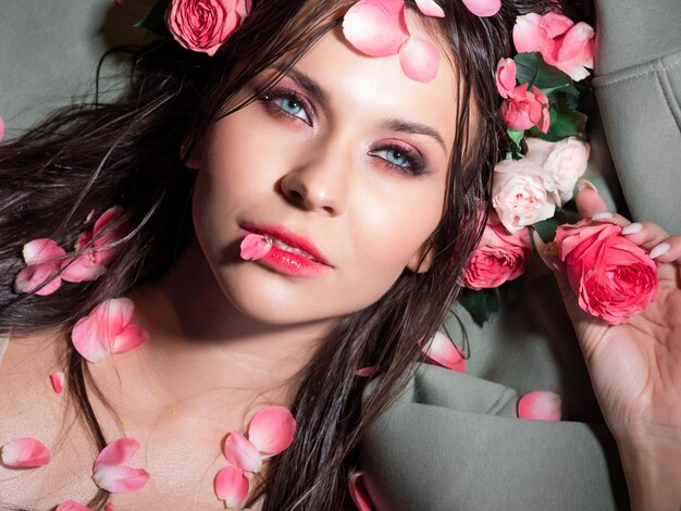 Beautiful blueeyed brunette with bright pink makeup lying sprinkled with pink rose petals closeup sp...