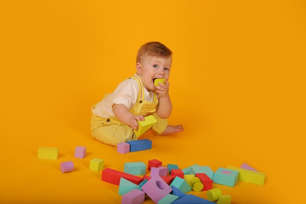 黄色いスーツを着た美しい青い目の小さな男の子は、カラフルなおもちゃで遊ぶ黄色