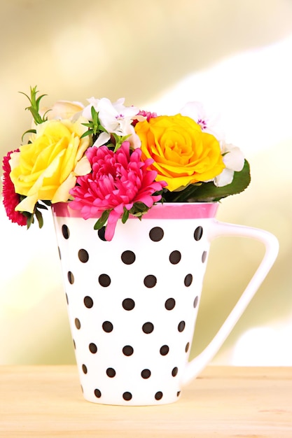 Foto bel bouquet di fiori luminosi in tazza di colore sulla tavola di legno su sfondo luminoso