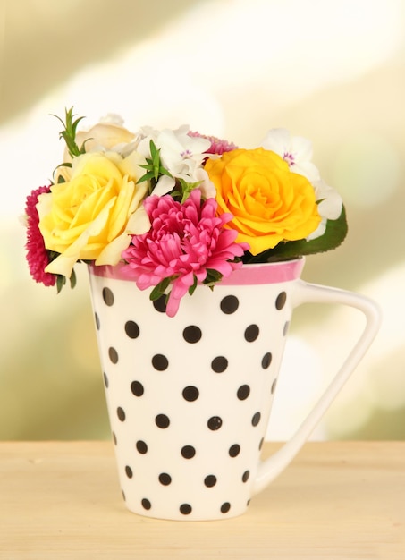 Beautiful bouquet of bright flowers in color mug on wooden table on bright background