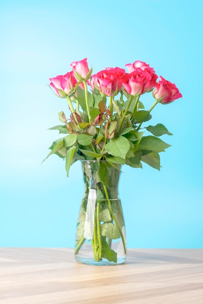 Beautiful bouquet of bright flowers in glass vase on blue background