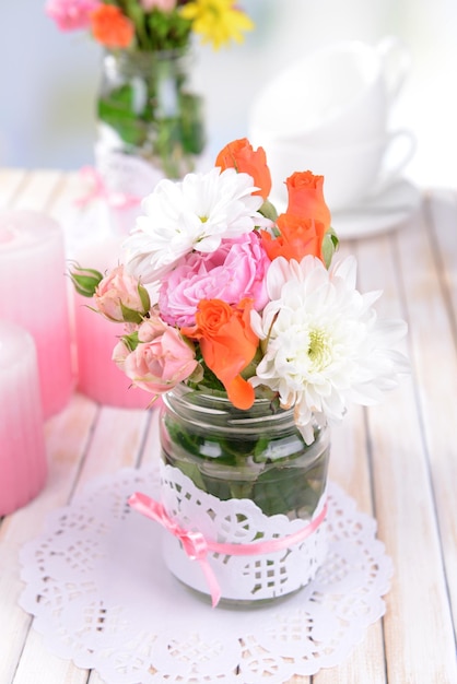 Beautiful bouquet of bright flowers in jars on table on light background