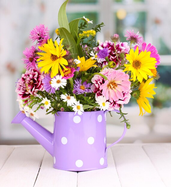 Beautiful bouquet of bright flowers in watering can on wooden table