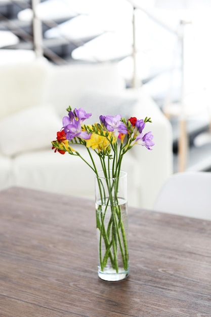 Beautiful bouquet of colorful freesias flowers on wooden table at living room