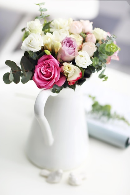 Beautiful bouquet of colourful roses in ceramic vase on white table