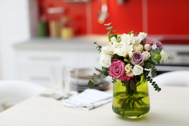 Beautiful bouquet of colourful roses in glass vase on the kitchen table