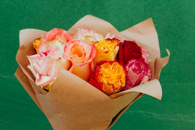  beautiful bouquet of fresh colorful roses packed in craft paper in front of the green wall