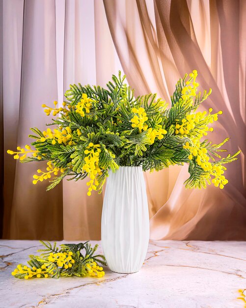 A beautiful bouquet of mimosa flowers in a white vase on the windowsill Spring still life
