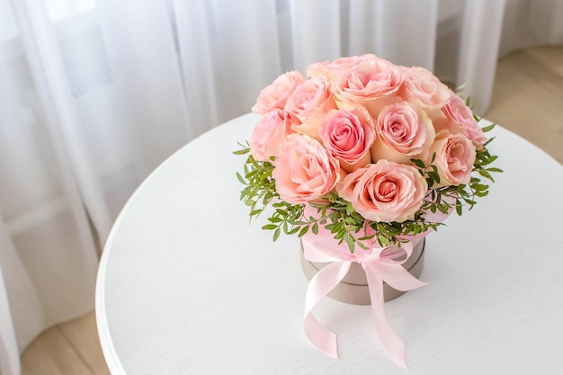 Красивый букет розовых роз в праздничной круглой коробке на белом столе.подарок на праздник, день рождения, свадьбу, день матери, день влюбленных,женский день. цветы в шляпной коробке.