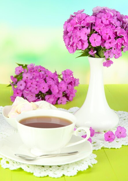 Beautiful bouquet of phlox with cup of tea on table on light background