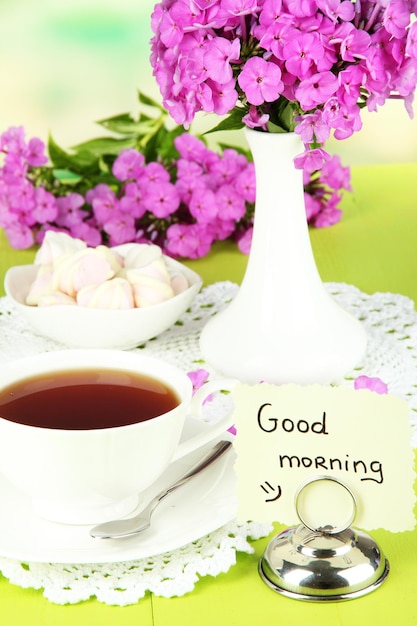 Beautiful bouquet of phlox with cup of tea on table on light background