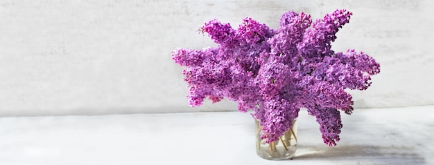 Beautiful bouquet of purple lilac on a glass jar ion white table