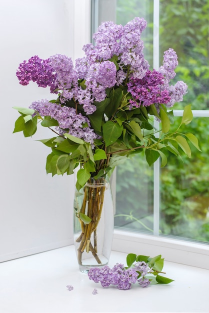 Beautiful bouquet of purple lilac in a glass vase on a white windowsill