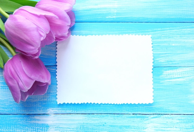 Beautiful bouquet of purple tulips and blank card on blue wooden background