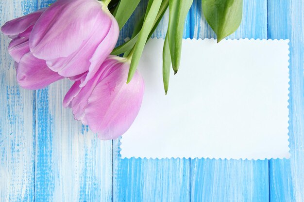 Beautiful bouquet of purple tulips and blank card on blue wooden background